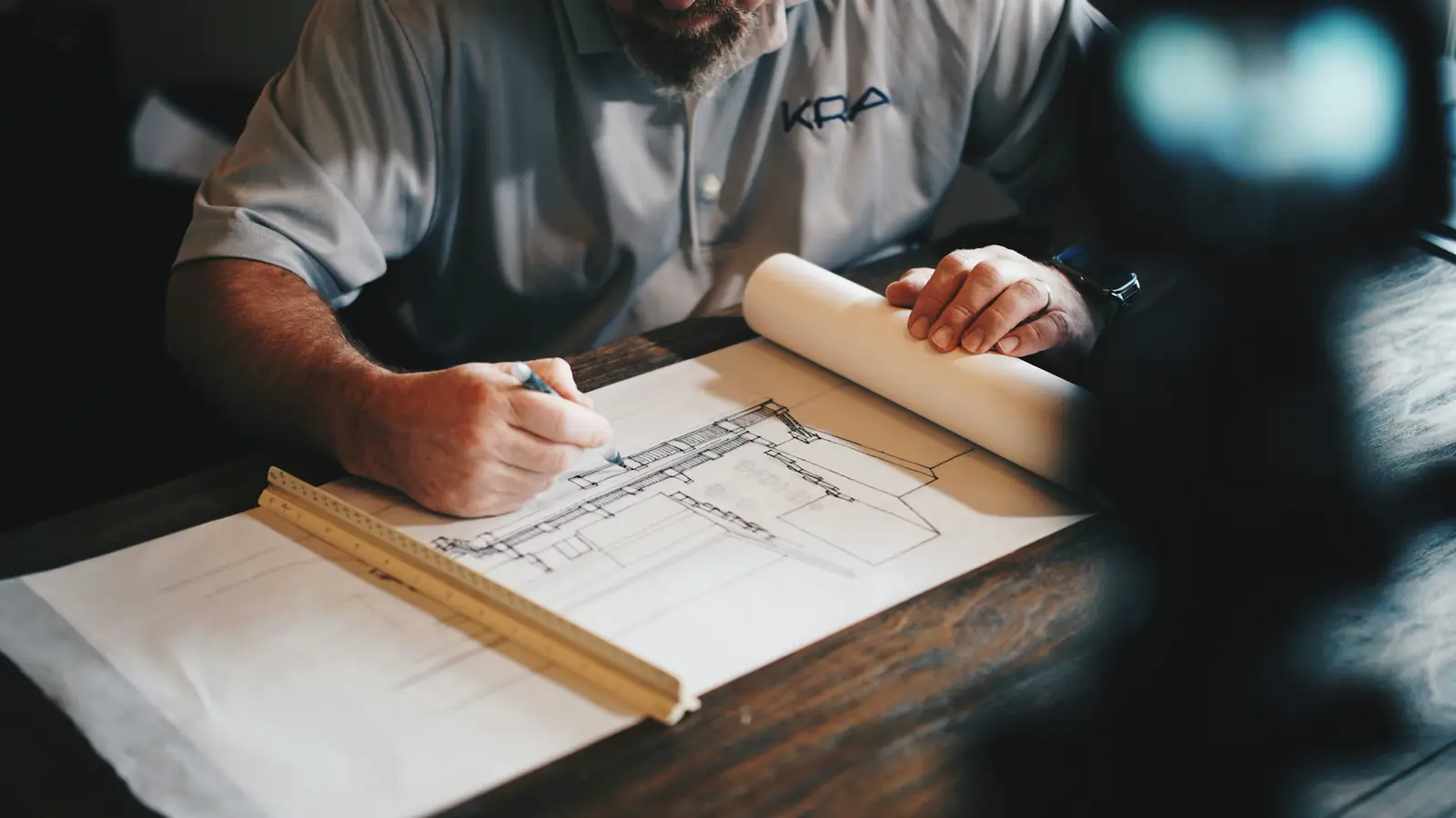 Hands and a pencil resting on architectural drawings spread across a table.