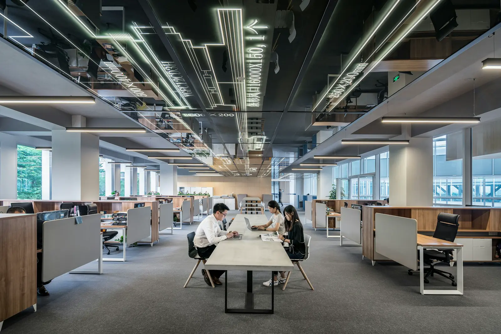 A man and a woman working on laptops at a long table in a wood-lined office.
